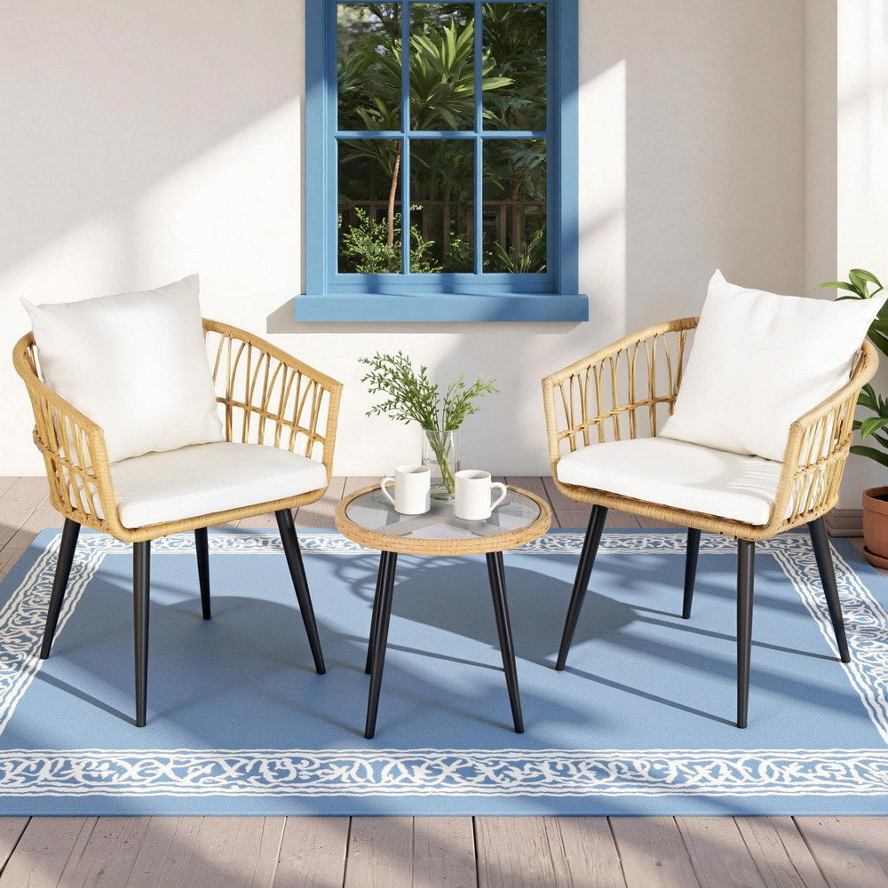 Two wicker chairs with white cushions and a matching table on a blue rug.
