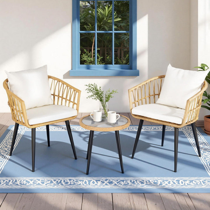 Two wicker chairs with white cushions and a matching table on a blue rug.